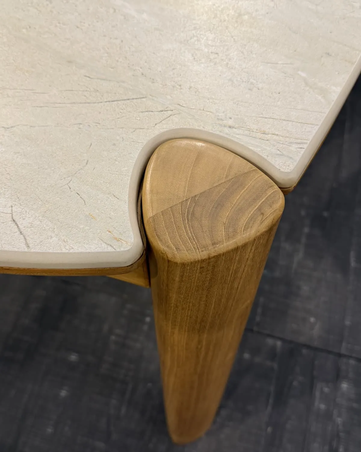 Table detail – a light stone top resting on a shaped teak leg